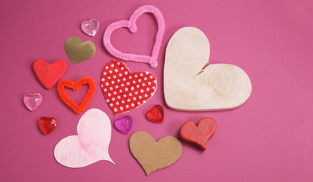 many of craft valentine hearts shapes made from different materials, wood plastic textile fabric, handmade creative gifts on pink background with copy spaceの写真素材