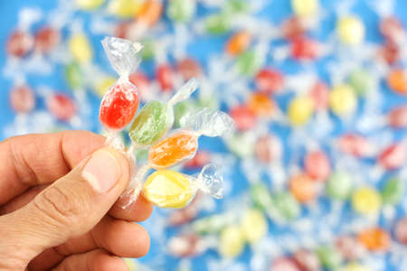 four different color sugar candies in hand on background of caramels or sweets, concept of childrens party or birthdayの写真素材