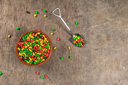 colored dragee in cup with teaspoon in shape of shovel full of candies, colorful sugar sweets mix, concept of sugar addiction, on wooden background with copy spaceの写真素材
