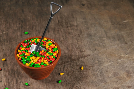 sunflower seeds in chocolate colored glaze in cup with teaspoon in shape of shovel, colorful sugar sweets mix, on wooden background with copy spaceの写真素材