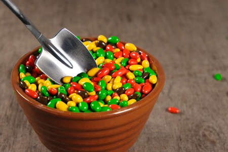 sunflower seeds in chocolate colored glaze in cup with teaspoon in shape of shovel, colorful sugar sweets mix, party or birthday food, on wooden background, close-up viewの写真素材