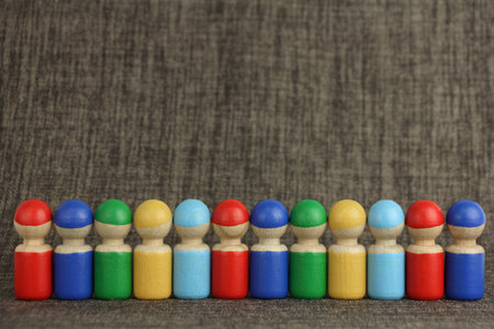 colorful wooden toy people are lined up in a row or queue, brown cloth or fabric background with copy space, concept of multinational friendship or teamworkの写真素材