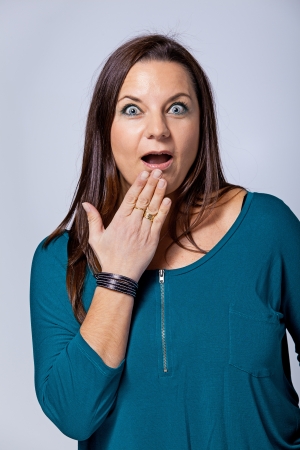 Surprised Mature Woman Covering her Mouth by Hand Over a Grey Backgroundの写真素材