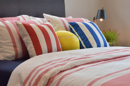 Modern bedroom interior with colorful pillows and reading lamp on bedside table