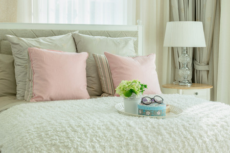 cozy bedroom interior with pink pillows and white tray of flower on bedの写真素材