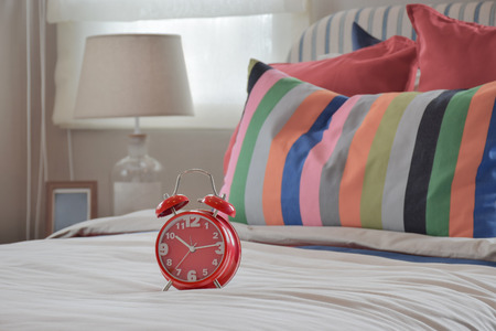 Red clock on white blanket and colourfull striped pillowsの写真素材