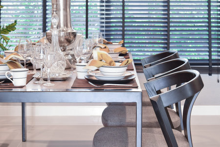 dining wooden table and comfortable chairs in modern home with elegant table setting