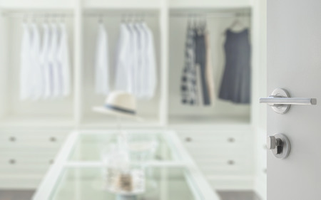 opened white door to walk in closet room with white hat and jewelry set on a dresser tableの写真素材