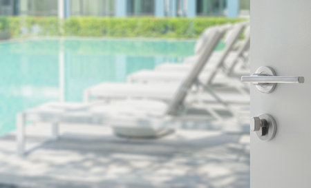 opened white door to swimming pool with beach chairsの写真素材