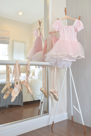 Girl's pink dress and ballet shoes hang on bar in bedroomの写真素材