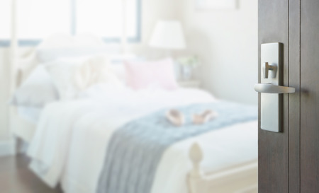 opened wooden door to bedroom with pillows and doll on white bedの写真素材