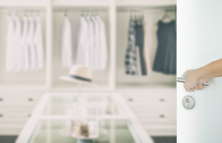 man hand opening white door to closet room with white shirt and hat on a tableの写真素材
