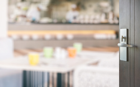opened wooden door to restaurant interior with colorful tables set for mealの写真素材