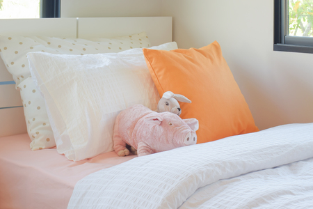 Piggy and rabbit doll setting on bed next to orange color pillow in cutie style bedroomの写真素材