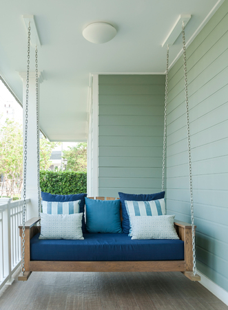 outdoor wooden porch swing bench with blue pillows.の写真素材