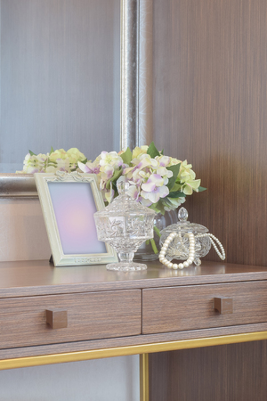 Jewelry crystal jar with picture frame and flowers on the wooden dressing tableの写真素材