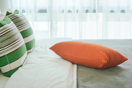 Orange pillow at center of bed in bedroomの写真素材