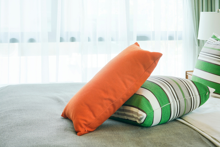 Orange pillow on green stripped pillows on bed next to windowの写真素材