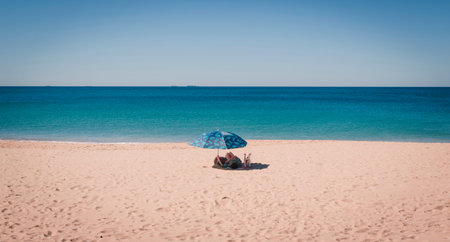 A girl in a swimsuit sunbathes on the beach under an umbrella.