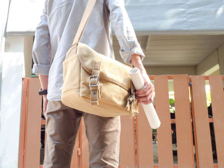 a man with messenger bag standing in front of the house and holding roll paperの写真素材