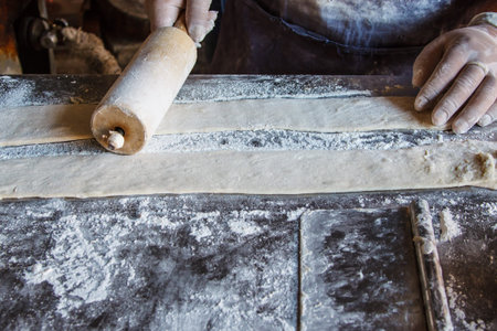 Female cook rolling dough with rolling-pin. Closeup view