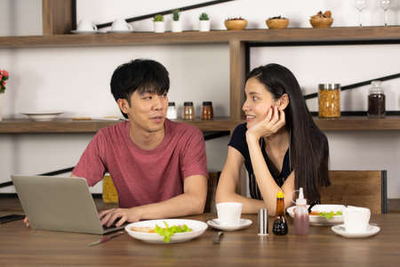 Asian young couple is feeding each other and smiling while cooking salad in kitchenの写真素材