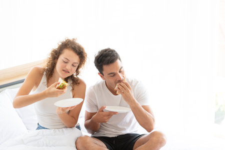 Happy couples relaxing in the white bedroom Of the apartment With various emotions With snacks, coffee, fruit in the morningの写真素材