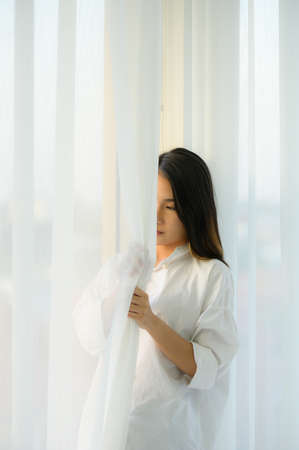 Young woman asian people in the bedroom with white curtains and the morning atmosphere when the sun shines.の写真素材