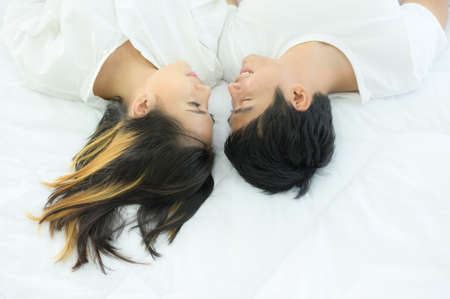 Couples are happy to relax in the white bedroom and share love with each other.の写真素材