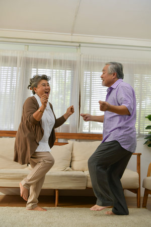 Spending time together at home, an elderly Asian couple having fun dancing in the living room.の写真素材