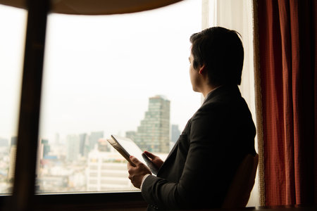 A young businessman monitors and keeps track of tasks in his office with a cityscape in the...