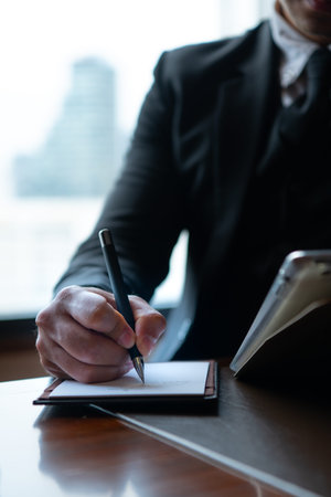 A young businessman monitors and keeps track of tasks in his office with a cityscape in the...