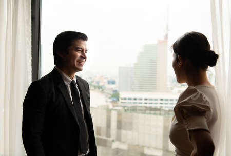 Two businessmen chat and follow up in their office with a view of the city behind their desks.の写真素材