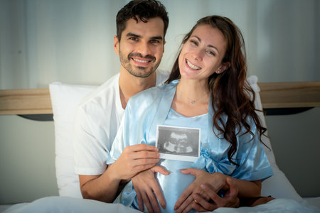 The happiness of a pregnant woman and her husband in the bedroom with the ultrasound film of the fetus that shows the results that the child is healthyの写真素材