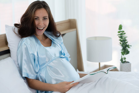 Pregnant woman in bedroom reading fairy tales to the baby in the womb in the morning after waking up