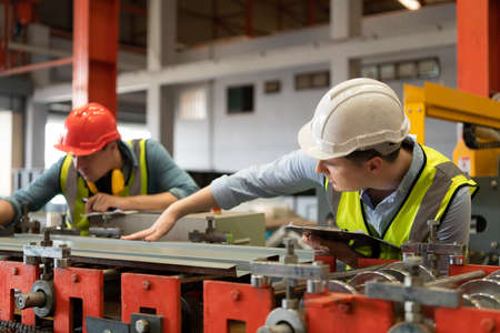 Two young engineers Testing and verifying the operation of the machines forming metal sheet tiles in the factoryの写真素材