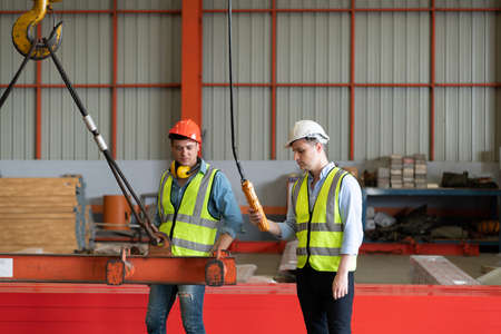 Two young engineers Testing and checking the operation of the over head crane in the factory.の写真素材
