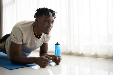 Young African man doing yoga exercise in the living room of his homewith the pleasure of relaxing with light sports In the morning atmosphere of the day.の写真素材