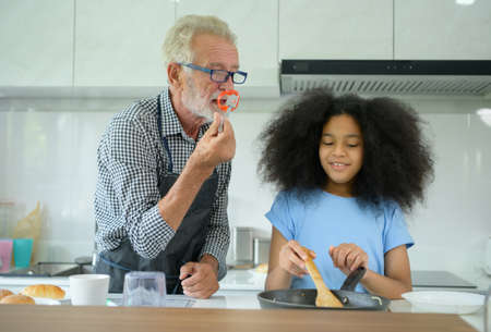 Family holiday activities with grandfather and grandchildren. Cooking dinner together for the family Grandfather is teaching cooking to his half-Asian granddaughter African Americanの写真素材