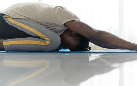 Young African man doing yoga exercise in the living room of his homewith the pleasure of relaxing with light sports In the morning atmosphere of the day.の写真素材