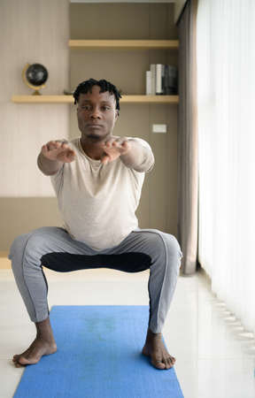 Young African man doing yoga exercise in the living room of his homewith the pleasure of relaxing with light sports In the morning atmosphere of the day.の写真素材