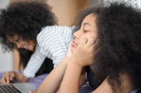 Asian-African American girls and sister Use a laptop to surf the Internet and  shop online. On the bed in bedroom in the holiday.の写真素材
