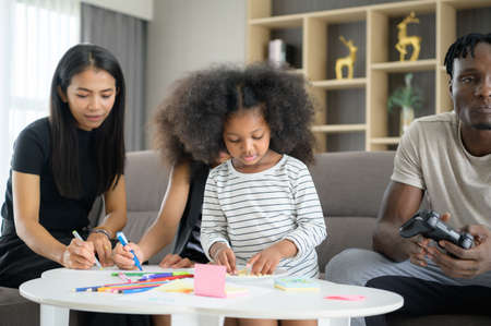 Asian-African American family relaxing, chatting, painting and having fun on vacation in the living room of the houseの写真素材