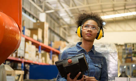 A young female worker is controlling a mechanical robot. to sort out the items that come into the warehouse to wait for the next shipment.の写真素材