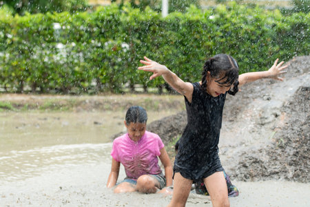 Little girls have fun playing in the mud in the community fields. with parents watching from a distanceの写真素材