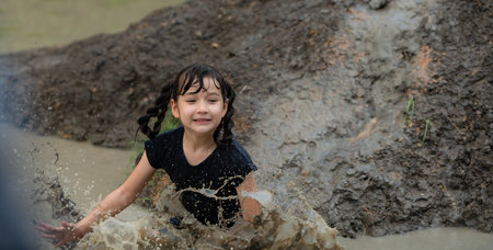 Little girls have fun playing in the mud in the community fields. with parents watching from a...