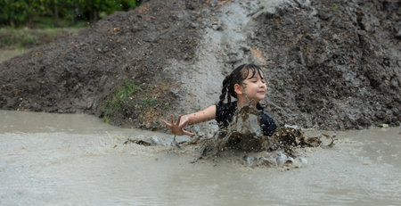 Little girls have fun playing in the mud in the community fields. with parents watching from a...
