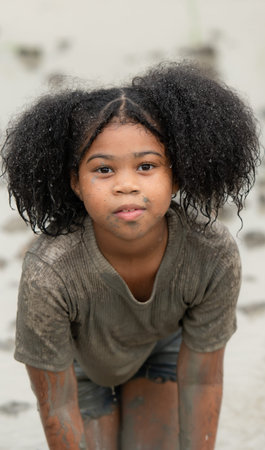 Little girls have fun playing in the mud in the community fields. with parents watching from a...