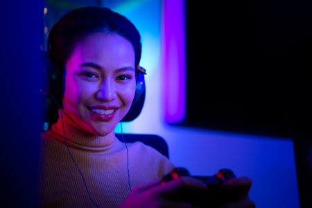 An active and serious young woman gamer on his powerful personal computer, playing first-person online video games. The game room includes a PC and bright neon LED lights.の写真素材