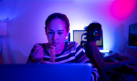Asian women who rely heavily on computers to watch drama series until having to eat instant noodles in front of it, The game room has computers and LED neon lights that are spectacular.の写真素材